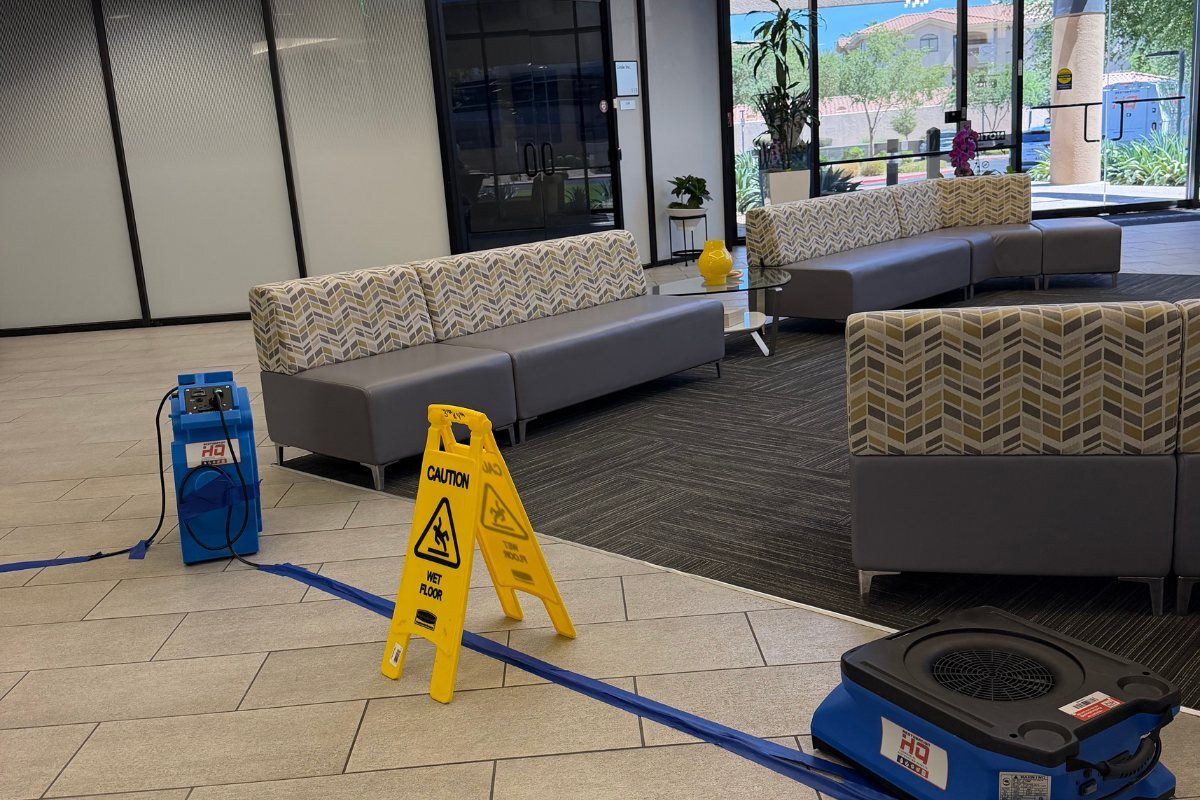 Air movers and a caution wet floor sign drying a commercial office lobby that remains open to occupants