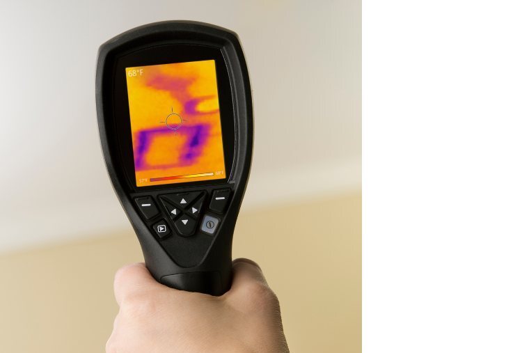 Technician holding a thermal imaging camera to locate hidden moisture behind a wall