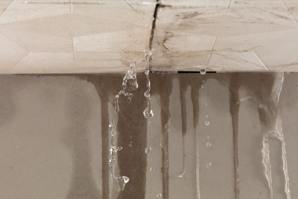 Water running down an interior wall from a failed ceiling above, with staining spreading across the surface